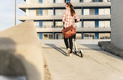 Young woman with headphones pushing electric scooter on parking deck