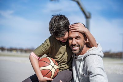 Portrait of happy father and son with basketball outdoors