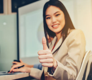 Portrait of smiling businesswoman gesturing thumbs up while working in office