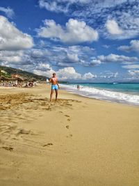 Boy walking on beach against cloudy sky