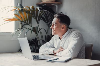 Side view of man using laptop while sitting on table