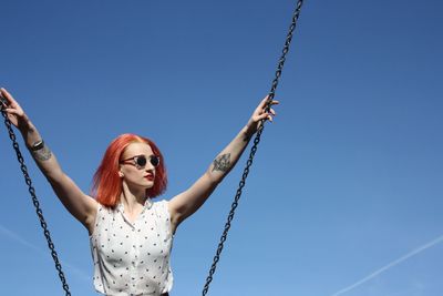 Portrait of young woman on swing against sky