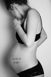 Side view of young pregnant woman standing against wall