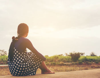 Rear view of woman sitting on field against sky