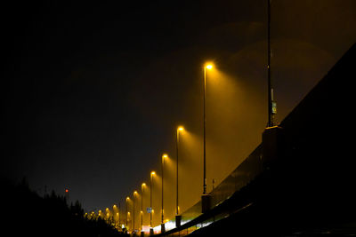 Illuminated street light against sky at night