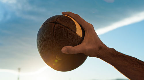 Cropped hand holding basketball against sky