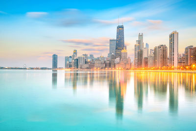 Scenic view of river by buildings against sky during sunset