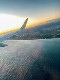 Airplane flying over sea against sky during sunset