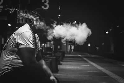 Side view of man smoking on road at night