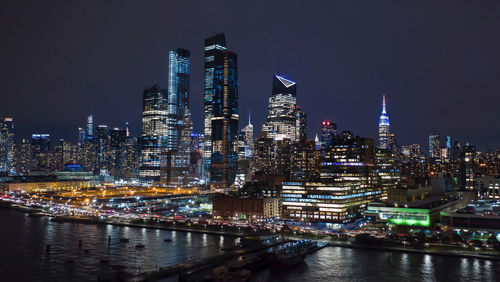 Illuminated buildings by river against sky at night