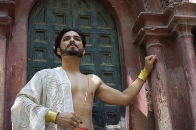 Young man looking away while standing against building