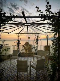 Chairs and tables by sea against sky at sunset