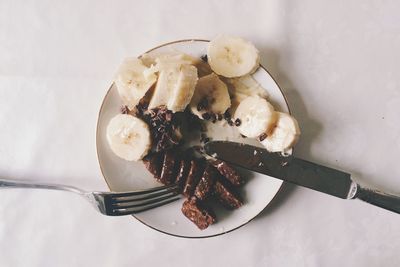 Directly above shot of banana slices and brownie in plate with fork and table knife