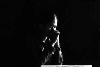 Woman praying while sitting against black background