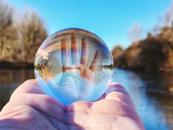 Close-up of hand holding crystal ball with reflection against river