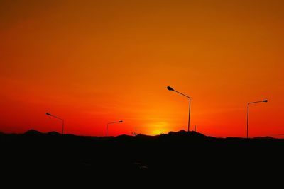 Silhouette cranes against orange sky