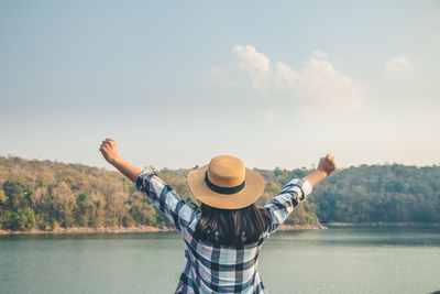 Rear view of woman standing by lake against sky