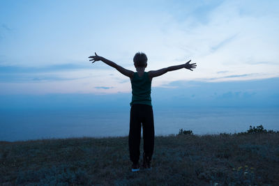 A child stands in a meadow with flowering herbs. the sea is visible in the distance. 