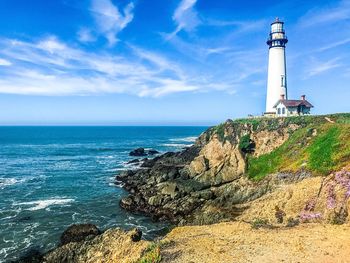 Lighthouse on cliff by sea against sky