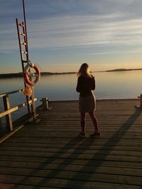 Rear view of woman standing on pier over sea against sky during sunset