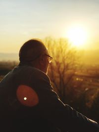 Man sitting on field against sky during sunset