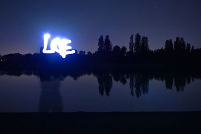 Silhouette trees by lake against sky at night