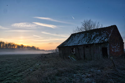 Abandoned house on field against sky at sunset