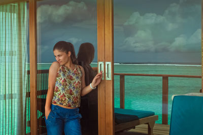 Beautiful woman standing by patio door with reflection of sea