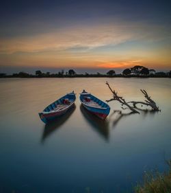 Boats moored in lake against sky during sunset