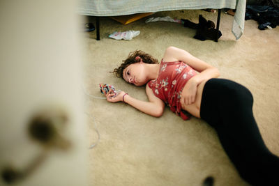 Teen girl lays on the carpeted floor of her room looking at her phone