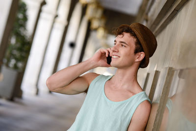 Young man talking on phone while standing by wall