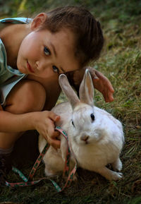 Portrait of cute girl with rabbit crouching on field