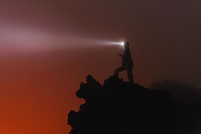 Woman with head torch standing against orange sky