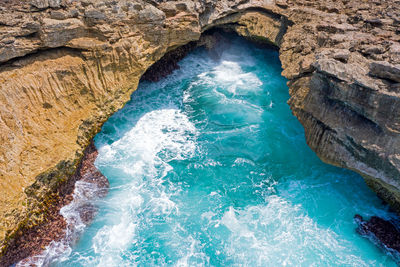 High angle view of waves splashing in sea by cliff