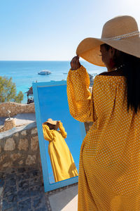 Beautiful african american woman in bright yellow dress admires in mirror on vacation by sea