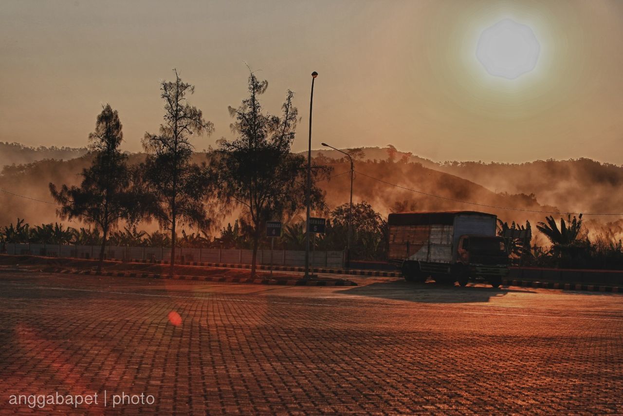 mountain, sunset, sky, road, transportation, street light, illuminated, landscape, sun, street, car, tree, tranquility, sunlight, nature, land vehicle, mountain range, tranquil scene, outdoors, no people