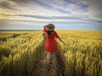 Rear view of woman wearing a red dress and a straw hat standingin a wheat field