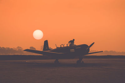 Side view of airplane at airport against orange sky