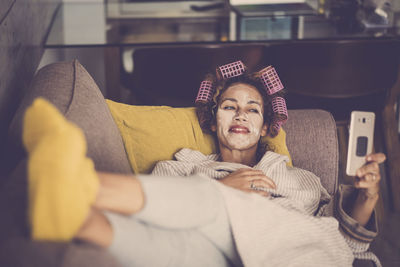 Smiling woman wearing facial mask taking selfie while relaxing at home