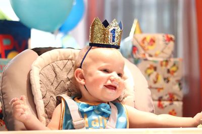 A baby boy smiles while he eats cake during his first birthday party.