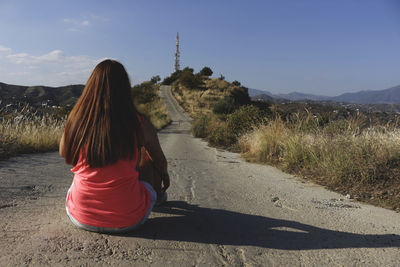 Rear view of woman sitting on road against sky