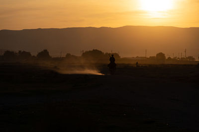 Silhouette man on field against sky during sunset