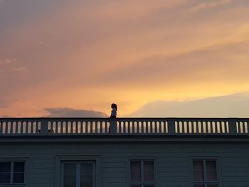 Low angle view of woman standing in balcony against sky during sunset