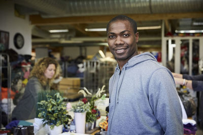 Portrait of confident mid adult man standing against colleagues working in warehouse