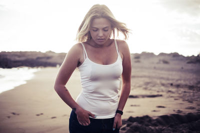 Young woman standing at beach against sky