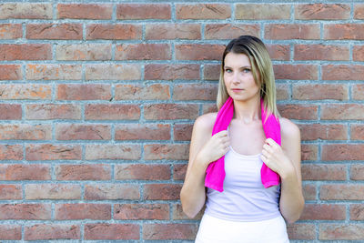 Portrait of young woman standing against brick wall