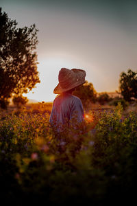 Man wearing hat standing amidst plants against clear sky at sunset