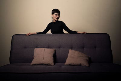 Portrait of woman sitting on sofa against wall
