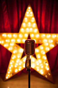 Close-up of microphone against illuminated light bulbs on star shape over stage