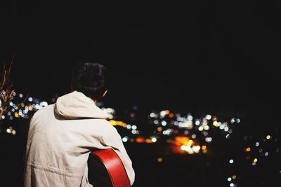 Rear view of man standing against illuminated city at night